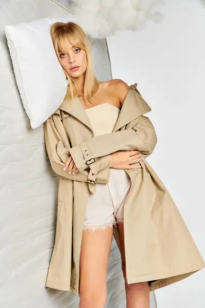 A stylish woman stands next to a matress, wearing a trench coat. — Stock Photo