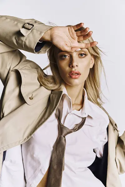 Stylish woman posing in trench coat and tie on white backdrop. — Stock Photo