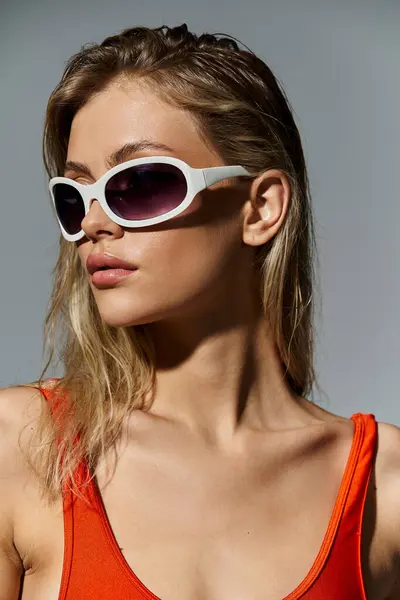 Mujer con estilo y cabello rubio con un top naranja y gafas de sol blancas. - foto de stock
