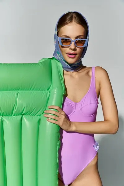 Fashionable blonde woman in purple swimsuit holding inflatable mattress. — Stock Photo