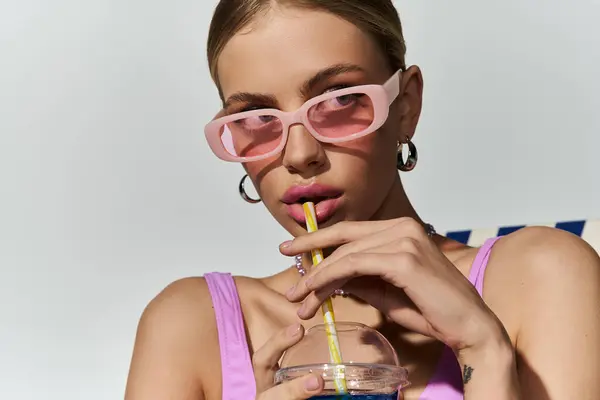 Mujer rubia en gafas de sol de color rosa sorbiendo una paja. - foto de stock