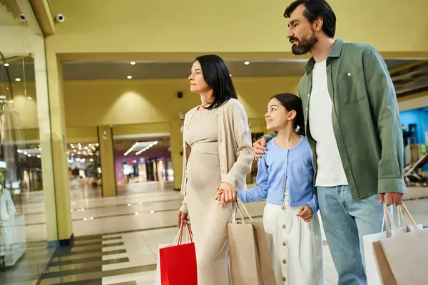 Una famiglia gioiosa, che trasporta borse della spesa, cammina insieme in un vivace centro commerciale. — Foto stock