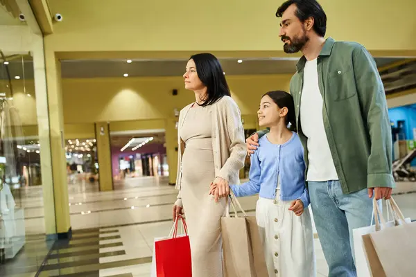 A joyful family, carrying shopping bags, walks together in a bustling shopping mall. — Stock Photo