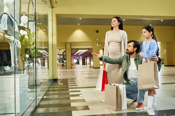 Una familia feliz examina sus bolsas de la compra en un centro comercial ocupado durante una excursión de fin de semana llena de diversión. - foto de stock