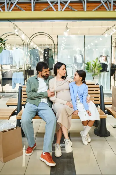 Une famille heureuse s'assoit sur un banc dans un centre commercial animé, profitant d'un moment de détente ensemble pendant leur sortie de week-end. — Photo de stock