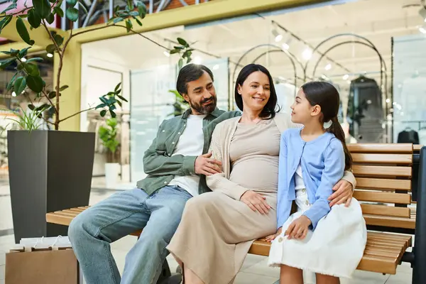 A cheerful family enjoys a shopping day, sitting together on a bench in a bustling mall. — Stock Photo