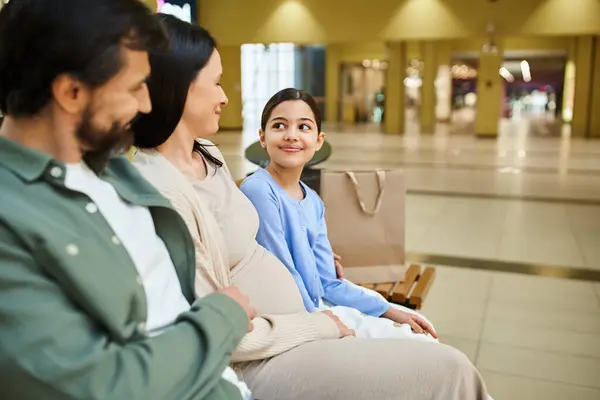 A content family enjoys a break on a bench in a bustling shopping mall during a fun weekend outing. — Stock Photo