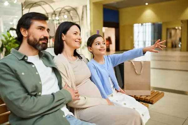 A happy family sits together on a bench, taking a break during a shopping outing in the mall. — Stock Photo