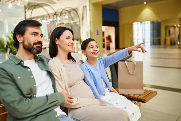 A cheerful family, enjoying a shopping weekend, relaxes on a bench in a bustling mall. — Stock Photo