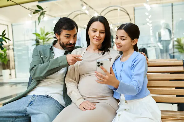 A family sits closely on a bench in a shopping mall, engrossed in a cell phone screen together. — Stock Photo