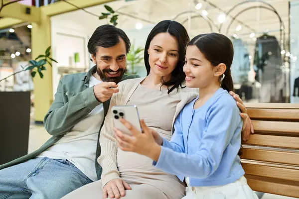 A happy family sits on a bench, engrossed in a cell phone together, enjoying a shopping weekend in the mall. — Stock Photo
