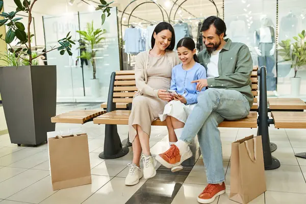 A happy family sitting together on a bench in a bustling shopping mall, enjoying a moment of rest and togetherness. — Stock Photo