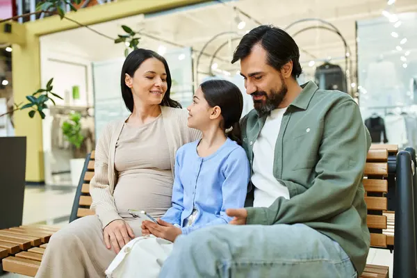 Une femme enceinte et sa fille partagent un moment joyeux assis sur un banc dans un centre commercial animé. — Photo de stock