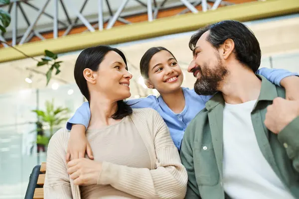 A joyful family sits together on a bench in a bustling shopping mall, taking a break from their shopping weekend. — Stock Photo