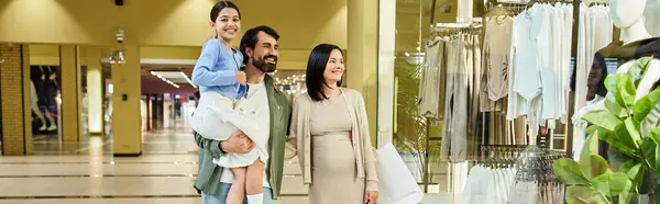 Счастливая семья, включая родителей и ребенка, идут вместе в оживленном торговом центре. — стоковое фото