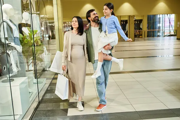 A pregnant woman and her husband walk together through a bustling shopping mall during a weekend outing. — Stock Photo