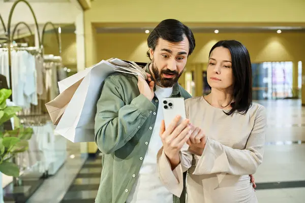 A man and woman engrossed in a cell phone at a bustling shopping mall. — Stock Photo