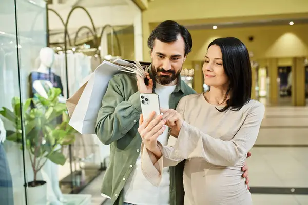 A man and woman absorbed in phone while walking in a busy shopping mall on a weekend outing. — Stock Photo