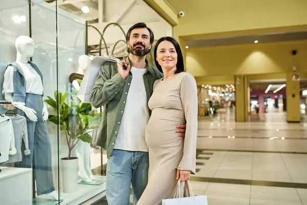 Une femme enceinte et un homme parcourent joyeusement les magasins ensemble dans un centre commercial animé le week-end. — Photo de stock