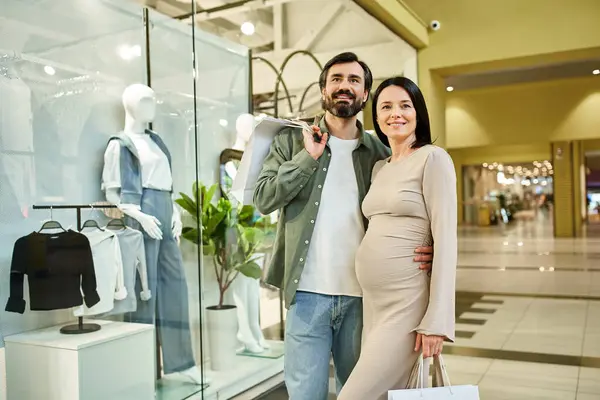 Una donna incinta e un uomo camminano insieme in un vivace centro commerciale, godendo di una gita di fine settimana. — Foto stock