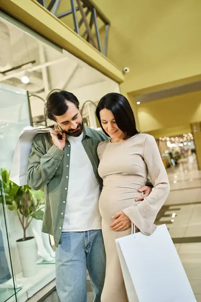 Una donna incinta con un sorriso luminoso tiene borse della spesa, godendo di una giornata al centro commerciale con la sua famiglia. — Foto stock