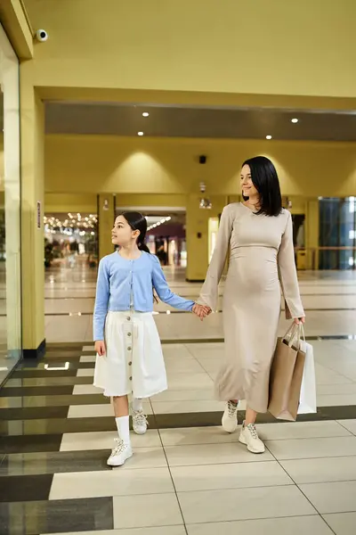 Uma mãe e filha alegremente segurar sacos de compras enquanto passeia por um shopping movimentado em um passeio de fim de semana cheio de diversão. — Fotografia de Stock
