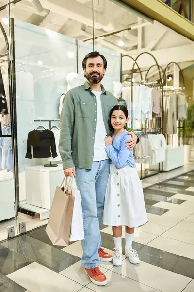 A man and his daughter stand together in a bustling shopping mall, enjoying a bonding moment on a weekend outing. — Stock Photo