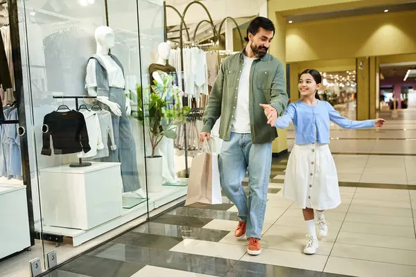 A father and his daughter walk together through a bustling shopping mall, enjoying a leisurely weekend outing. — Stock Photo
