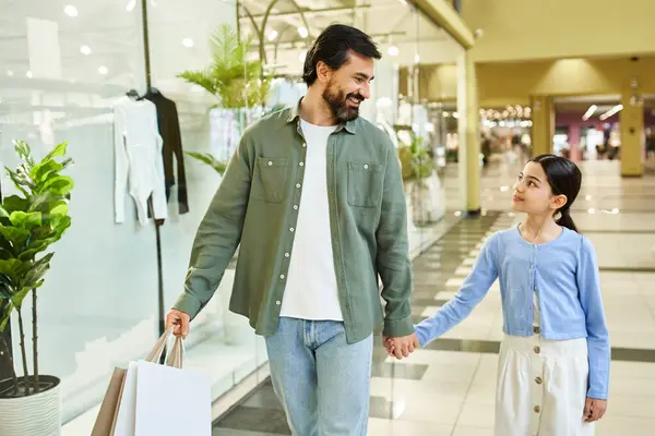 A man and a girl happily walk through a mall, holding shopping bags filled with purchases. — Stock Photo