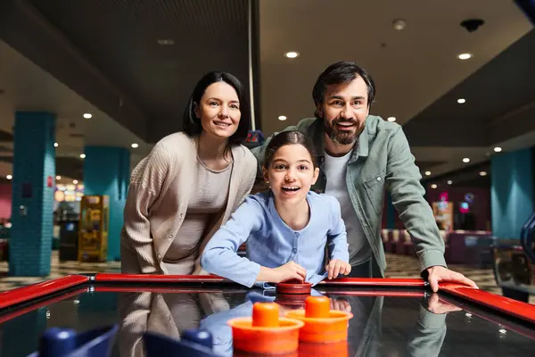 A happy family competes in a game of air hockey at an arcade, laughing and enjoying a fun weekend together. — Stock Photo