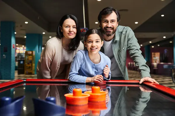 A happy family enjoying a competitive game of air hockey in a lively mall gaming zone on the weekend. — Stock Photo