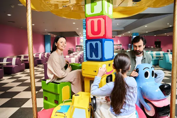 A happy family playing with a toy carousel in a lively gaming zone during a fun weekend outing. — Stock Photo