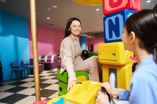 A woman joyfully plays with a child in a vibrant toy room, surrounded by colorful toys and games. — Stock Photo