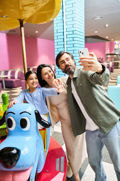 A happy family cherishes a selfie moment while surrounded by a toy carousel in a mall gaming zone on a weekend. — Stock Photo