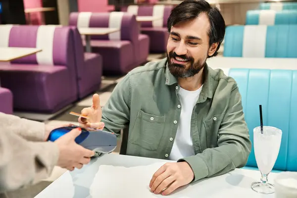 A man offers his credit card to waitress at a restaurant, paying for milkshake — Stock Photo