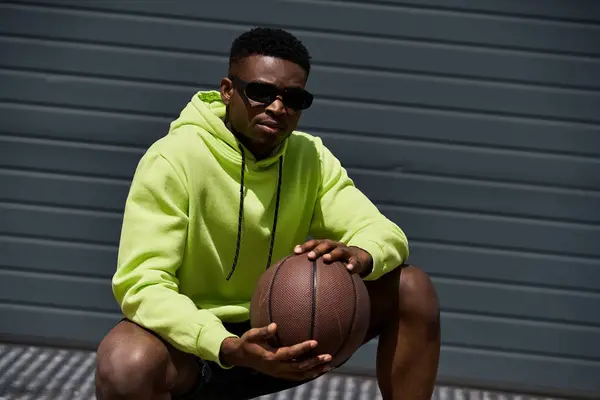 Schöner afroamerikanischer Mann im trendigen grünen Kapuzenpulli hält einen Basketball in der Hand. — Stockfoto