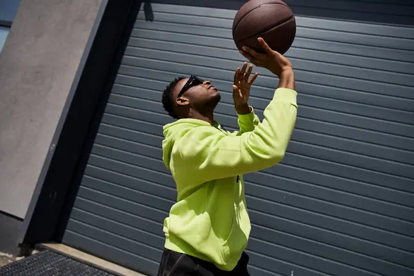 Schöner Mann in grünem Kapuzenpulli fängt Basketball. — Stockfoto