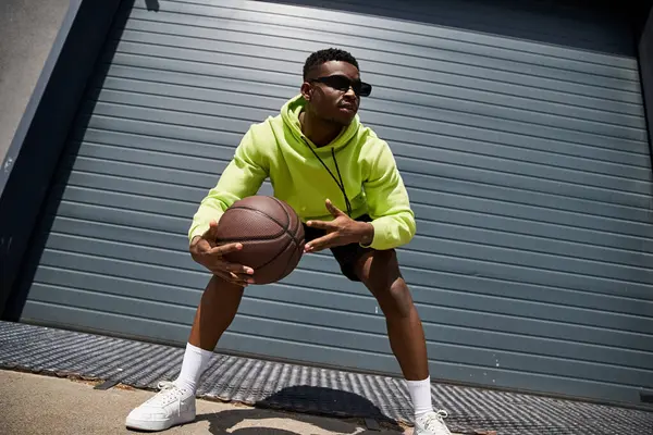 Ein stylischer afroamerikanischer Mann in grünem Kapuzenpulli hält einen Basketball in der Hand. — Stockfoto