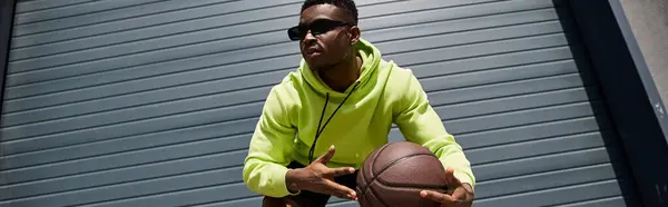 Afroamerikaner in grünem Kapuzenpullover hält Basketball. — Stockfoto