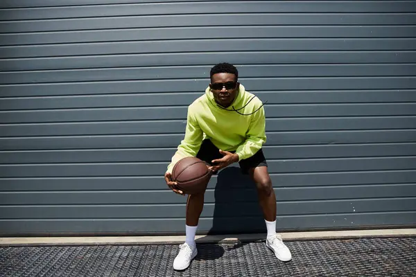 Модный молодой человек в зеленой толстовке держит баскетбол. — стоковое фото