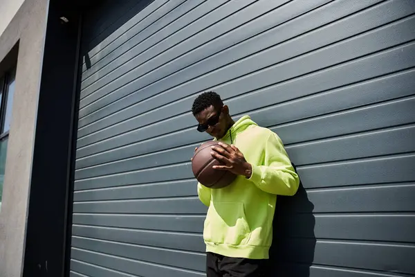 Stylish African American male in yellow hoodie, gripping basketball. — Stock Photo