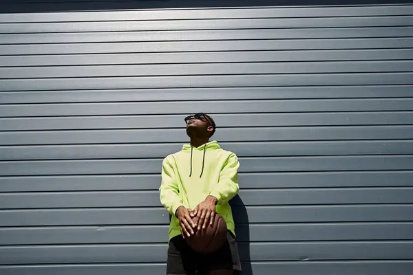 Афроамериканец в модной желтой толстовке держит баскетбол — стоковое фото