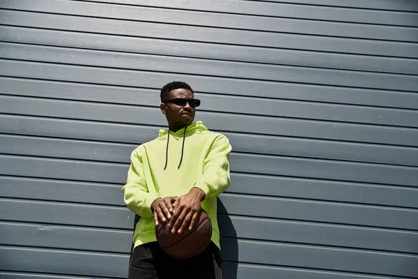 Stylish African American man leans against a wall in a bright neon yellow hoodie. — Stock Photo