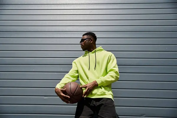 Стильный афроамериканец в неоновой толстовке держит баскетбол. — стоковое фото