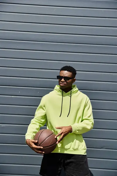 Junger Afroamerikaner in neongrünem Kapuzenpulli hält Basketball in der Hand. — Stockfoto
