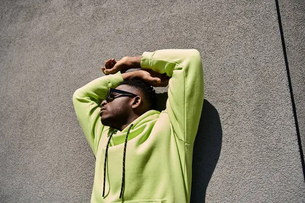 Stilvoller afroamerikanischer Mann lehnt im lindgrünen Kapuzenpullover an einer Wand. — Stockfoto