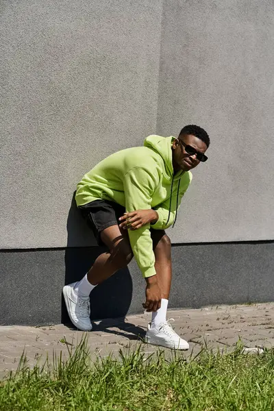 Stylish African American man in green hoodie leaning against a wall. — Stock Photo