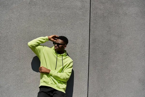 Stylish young man in neon hoodie leaning against wall. — Stock Photo