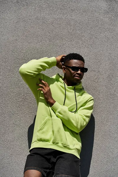 Handsome African American man in lime green hoodie leaning against wall. — Stock Photo