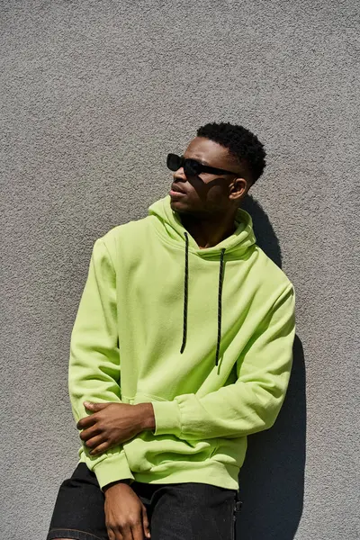 Handsome African American man leans against a wall in a lime green hoodie. — Stock Photo